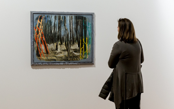 The picture shows a woman in front of a painting by Markus Lüperz