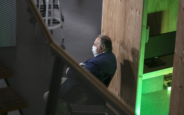 Peter Weibel sitzt mit einer Mund-Nasen-Schutz-Maske auf einem Stuhl und schaut aus dem Bild raus.