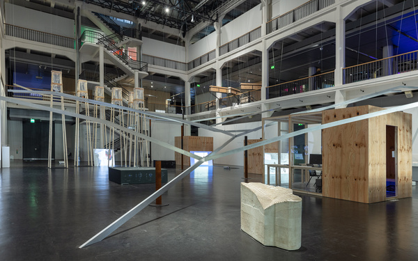 Blick in den Lichthof und auf die Installation, die sich durch den ganzen Lichthof erstreckt. Ein Metallgerüst deutet die Topologie des Strengbach Observatorium an. Im Raum verteilt sind Bildschirme mit Videos zu sehen.
