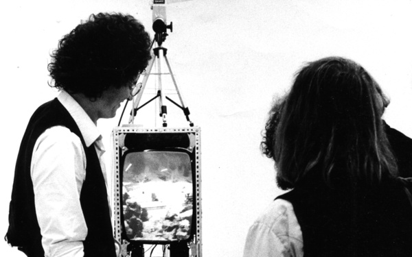 Drei Personen blicken auf eine Video-Installation mit zwei Monitoren und einer Kamera