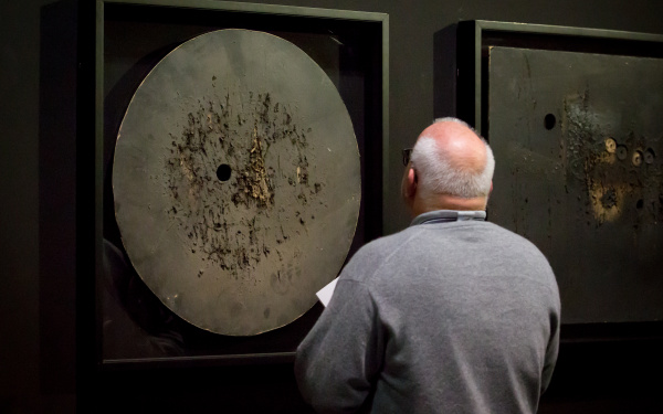  The photo shows the back of a bald man in front of a work by Aldo Tambellini.