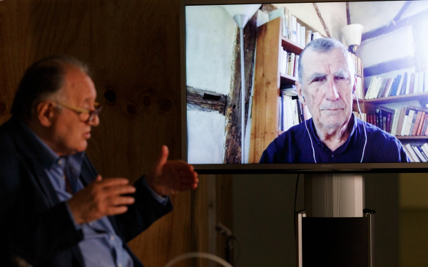 Peter Weibel sitzt vor einem großen Bildschirm auf dem Bruno Latour zu sehen ist.