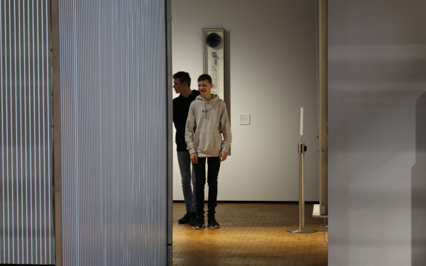 Zwei Jungs laufen mit geschlossenen Augen durch die Ausstellung »Writing the History of the Future«.