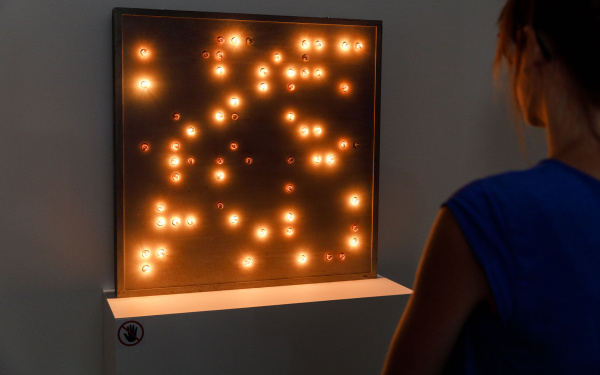 A woman stands in front of a reddish box with dots of light