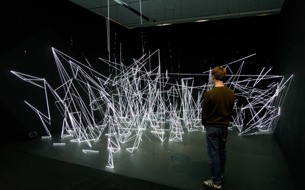 An installation of white, illuminated nylon threads in geometric shapes.