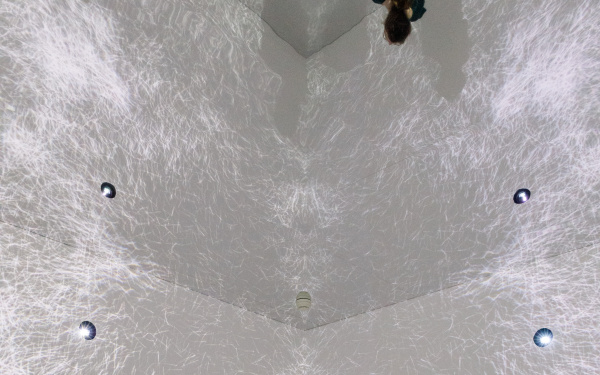 Visitors in a room with video projections on walls and ceiling and a mirrored floor.