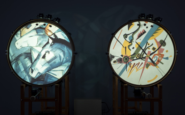 You can see two standing drums, each showing a picture of different shapes on the round surface. On the left drum a horse's head is recognizable from the forms. 