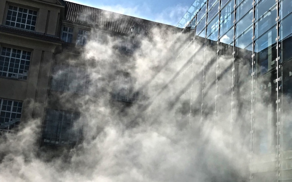 A sculpture of fog encloses a glass building.