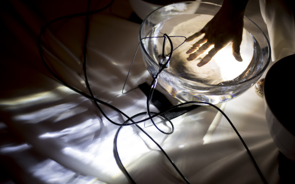 Foto einer Hand in einer Glasschale, die mit Wasser gefüllt ist. In der Schale hängt ein Mikrofon.