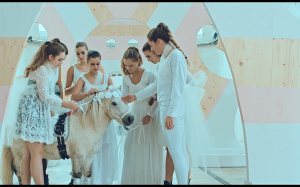 The photo shows a white pony surrounded by seven girls in white clothes.