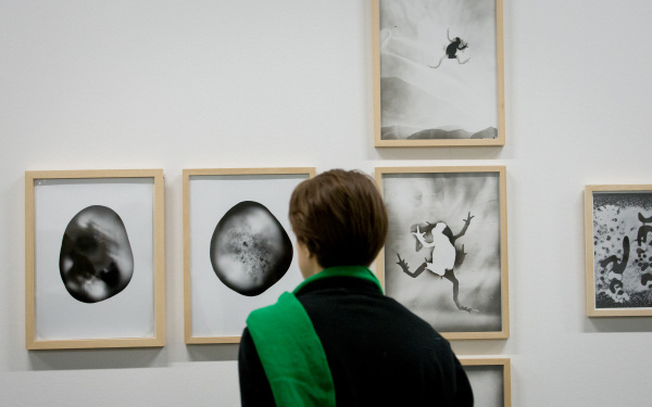 A woman with a green scarf looks at several black and white images on a wall