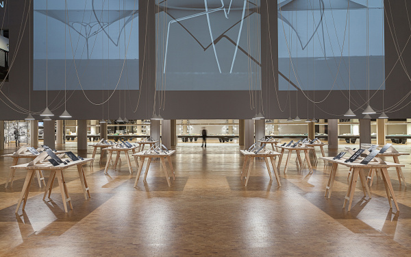 Frei Otto Ausstellungsansicht: Tische mit Schwarzweißfotos, hängenden Seilen und einem raumfüllenden Screen
