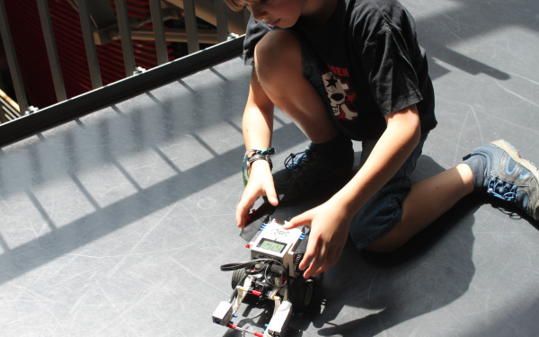 Ein Junge kniet auf dem Boden neben einem Lego-Roboter.