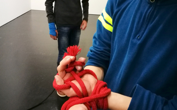 Zu sehen sind die Hände eines Schülers mit einem roten Seil geknebelt im Rahmen der Veranstaltung »Art im Puls«.