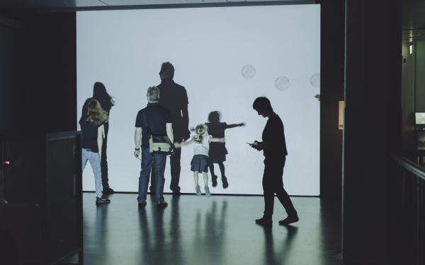 Museumsbesucher bewegen sich vor einer Leinwand mit Seifenblasen 