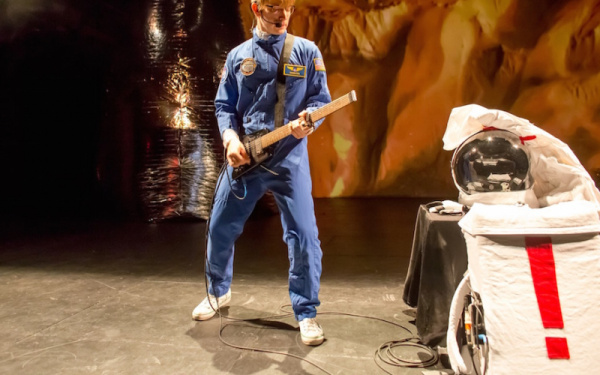 You can see a young man in a blue astronaut suit and a guitar in his hand.