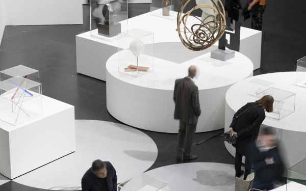 Sculptures stand on white pedestals, visitors are on their way in between.
