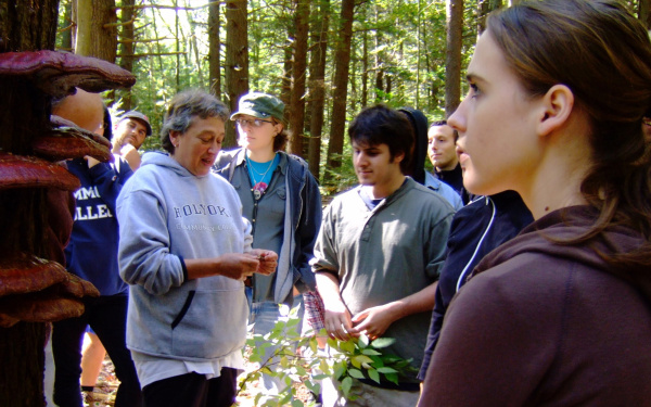 Lynn Margulis stands in the forest and explains something to a group of students.