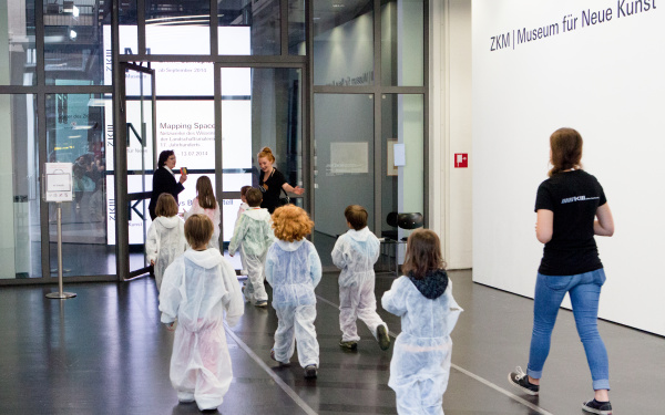 Kinder in weißen Overalls betreten das Museum für Neue Kunst