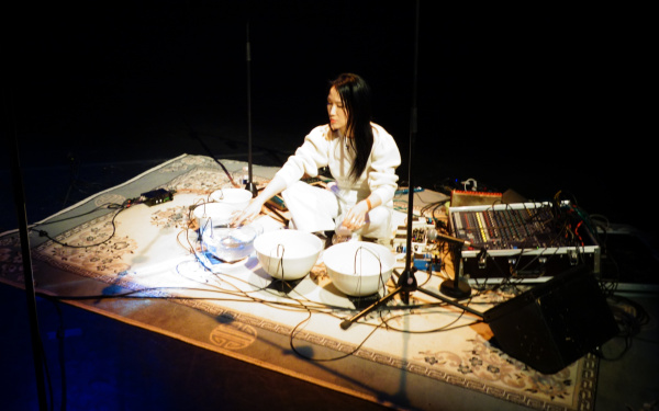 Tomoko Sauvage sitzt auf dem Boden, vor ihr stehen mit Wasser gefüllte Schalen und Mikrofone.