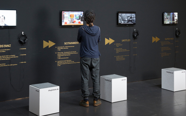 Ausstellungsansicht von »Fast Forward Science«: Eine Wand mit Monitoren, davor ein junger Mann.