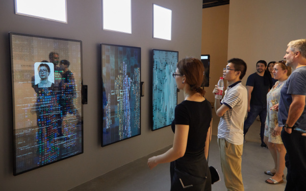 Eine Frau steht vor dem Kunstwerk YOU:R:CODE bestehend aus großen Bildschirmen