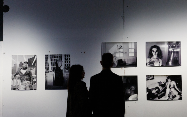 Two people, which can only be racognised as shadows, are standing in front of a wall with several black and white photographies.