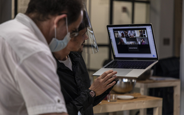 Ein Mann hält seinen Laptop hoch und zeigt anderen Teilnehmer:innen in einer Videokonferenz, was der Mann neben ihm vor sich hat.