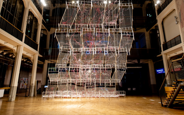 Installationsansicht von Chiharu Shiota`s Werk »Connected to Life«. Zu sehen sind aneinandergereihte, miteinander verbundene Bettgestelle, durchzogen von roten Schläuchen, die sich immer weiter vom Boden abheben und gemeinsam eine Art Weg aufwärts bilden.