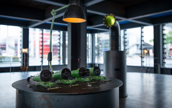 Under a lamp, 3 tubular sockets lie on a metal desk in a glassed-in showroom.