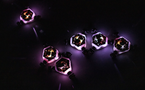 Glowing little robot spinning tops move on a dark background and interact with each other.