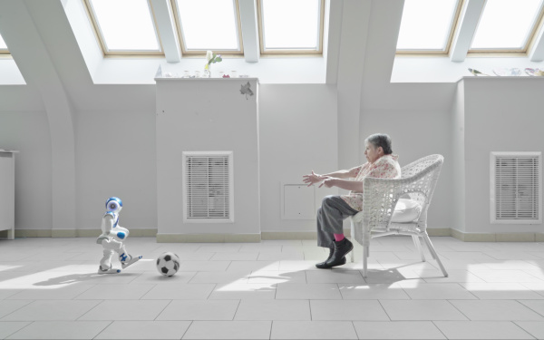 Ein kleiner humanoider Roboter spielt Fußball mit einer Seniorin in einem Pflegeheim.