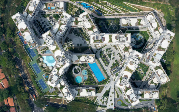 Das Foto zeigt einen großen Gebäudekomplex aus der Vogelperspektive. Von Oben sieht man wie verwinkelt die Stockwerke aufeinander aufbauen und zwischendrin erkennt man viel Grün und Pools.