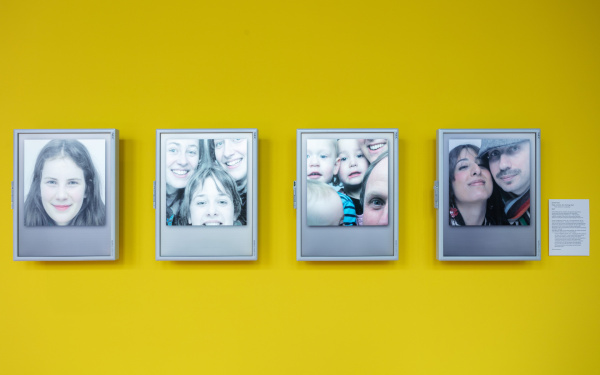 gelbe Wand mit vier Monitoren, die Gesichter zeigen
