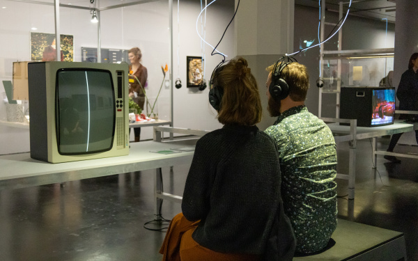 Ausstellungsansicht »Matter. Non-Matter. Anti-Matter« im ZKM | Zentrum für Kunst und Medien Karlsruhe, 2022. Zu sehen sind zwei sitzende Personen mit dem Rücken zur Kamera. Sie tragen Kopfhörer.