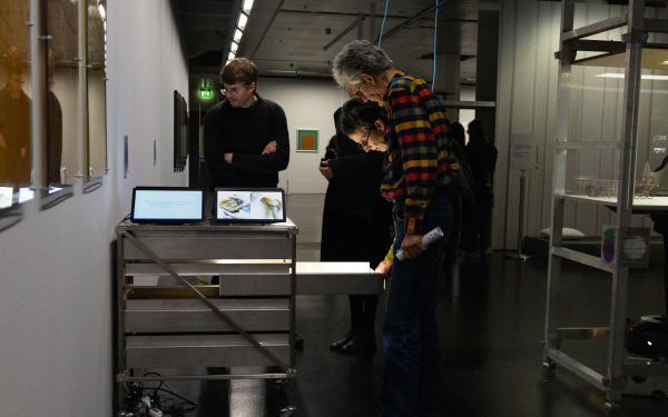 Ausstellungsansicht »Matter. Non-Matter. Anti-Matter« im ZKM | Zentrum für Kunst und Medien Karlsruhe, 2022. Zu sehen sind Personen um einen Wagen herum, auf dem Tablets sind. Zwei Personen haben eine Schublade geöffnet und betrachten deren Inhalt.