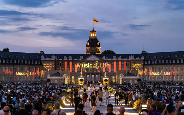 Zu sehen ist die Eröffnung der Schlosslichtspiele. Das Schloss Karlsruhe leuctet unter dem Motto Musik 4 Life, welches an die Fassade projeziert ist.