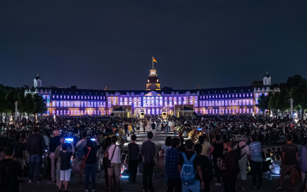 Der schwarze Himmel als Hintergrund hebt das hell erleuchtete Schloss hervor. Das Karlsruher Schloss erleuchtet in verschiedenen lila und rosa Tönen und nutzt die Strukturen des Schlosses aus, um geometrische Muster zu erzeugen.