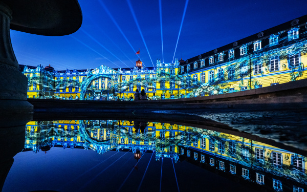 Zu sehen ist die beleuchtete Fassade des Karlsruher Barockschlosses in den Farben Blau und Gelb.