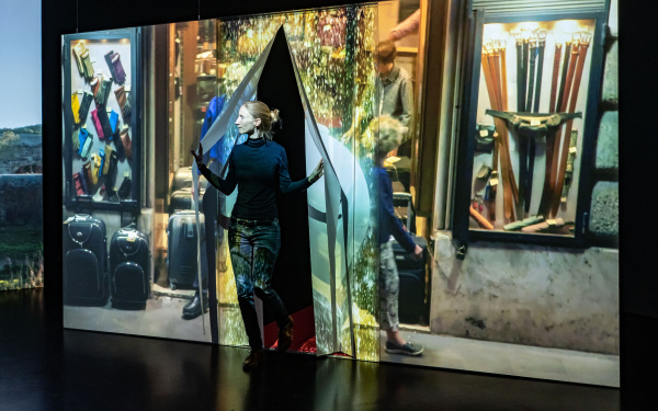 Ausstellungsansicht »Marijke van Warmerdam. Then, now, and then«. Zu sehen ist eine Person, die durch einen Vorhang tritt, auf dem ein Video projiziert wird.
