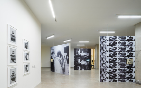 Zu sehen ist ein Ausstellungsraum. Drei große schwarz-weiß Bilder teilen den Raum auf. Links an der Wand hängen 6 schwarz-weiß Fotografien in weißen Bilderrahmen.