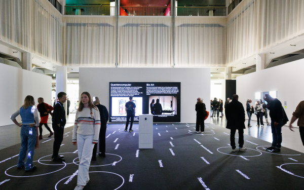 You can see several people on a black surface. On this surface there are words. Around the people are white circles. In the background are two screens.