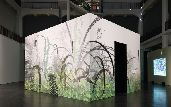 On display is the work "Interactive Plant Growing". An exterior view shows the work from the outside. A cube inside of which are the plants. The cube is decorated with floral pattern from the outside. It stands in the middle of the exhibition space.