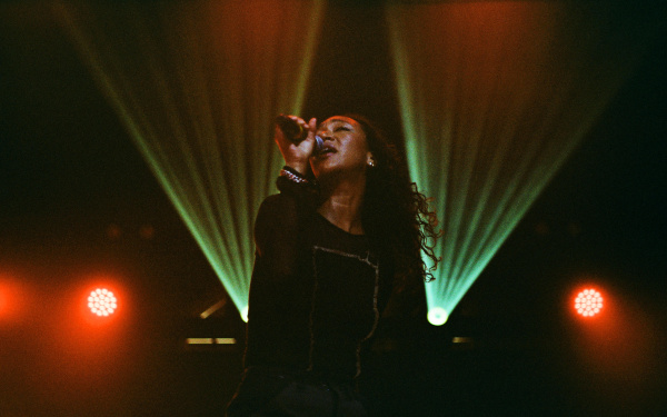 Sophia Mitiku during a performance with microphone on a dark stage with green and red light