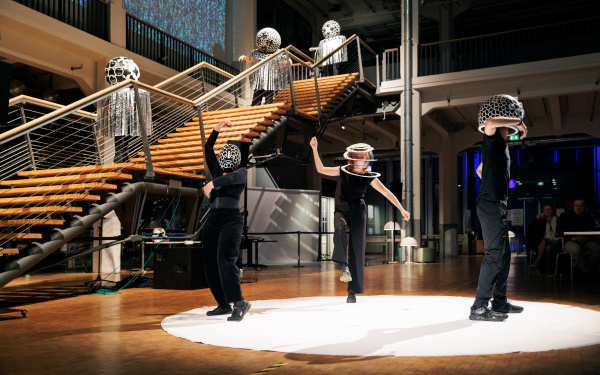 Fünf verkleidete Menschen tanzen ihre performance im Foyer des ZKM. Ihre Verkleidung besteht aus einer geschmückten Kugel über ihrem Kopf, sonst sind sie schwarz angeszogen.