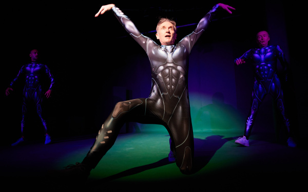 A man in futuristic armor strikes a pose in the spotlight on stage.