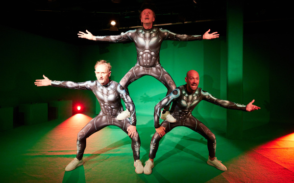 Three men in futuristic armor make a human pyramid in a green screen studio