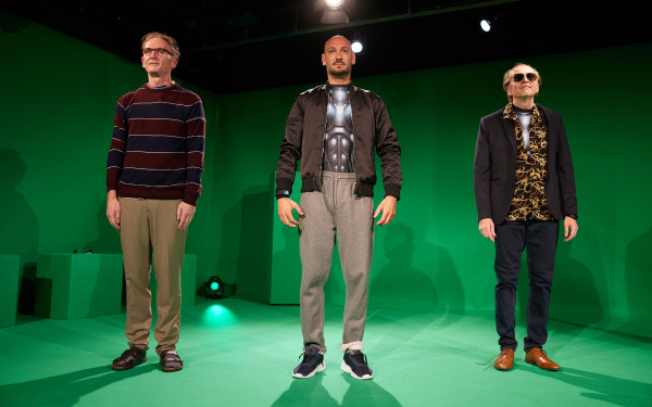 Three men in futuristic armor stand in a green-screen studio