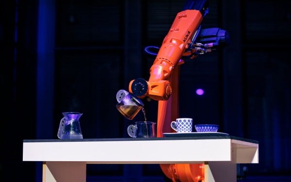 Ein orangener Roboter schenkt Tee in eine kleine Tasse ein.