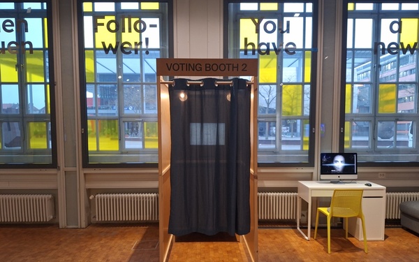 Ansicht einer Wahlkabine aus Holz mit blauem Vorhang.